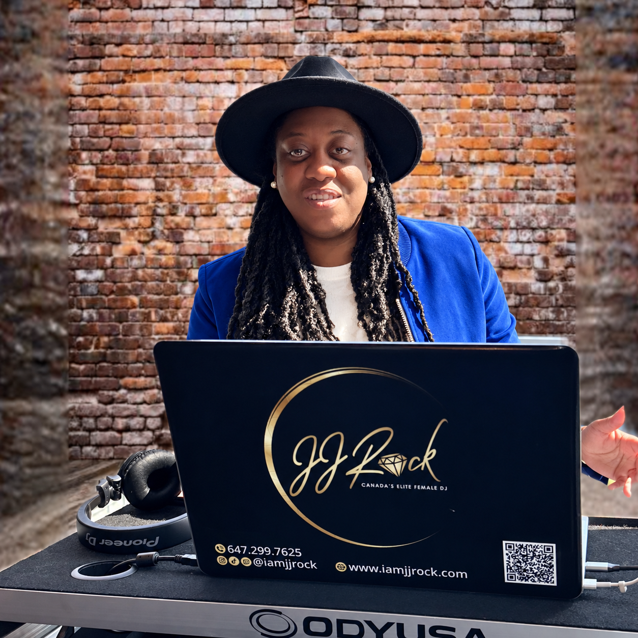 DJ JJ Rock in a blue blazer and black hat at her branded DJ setup