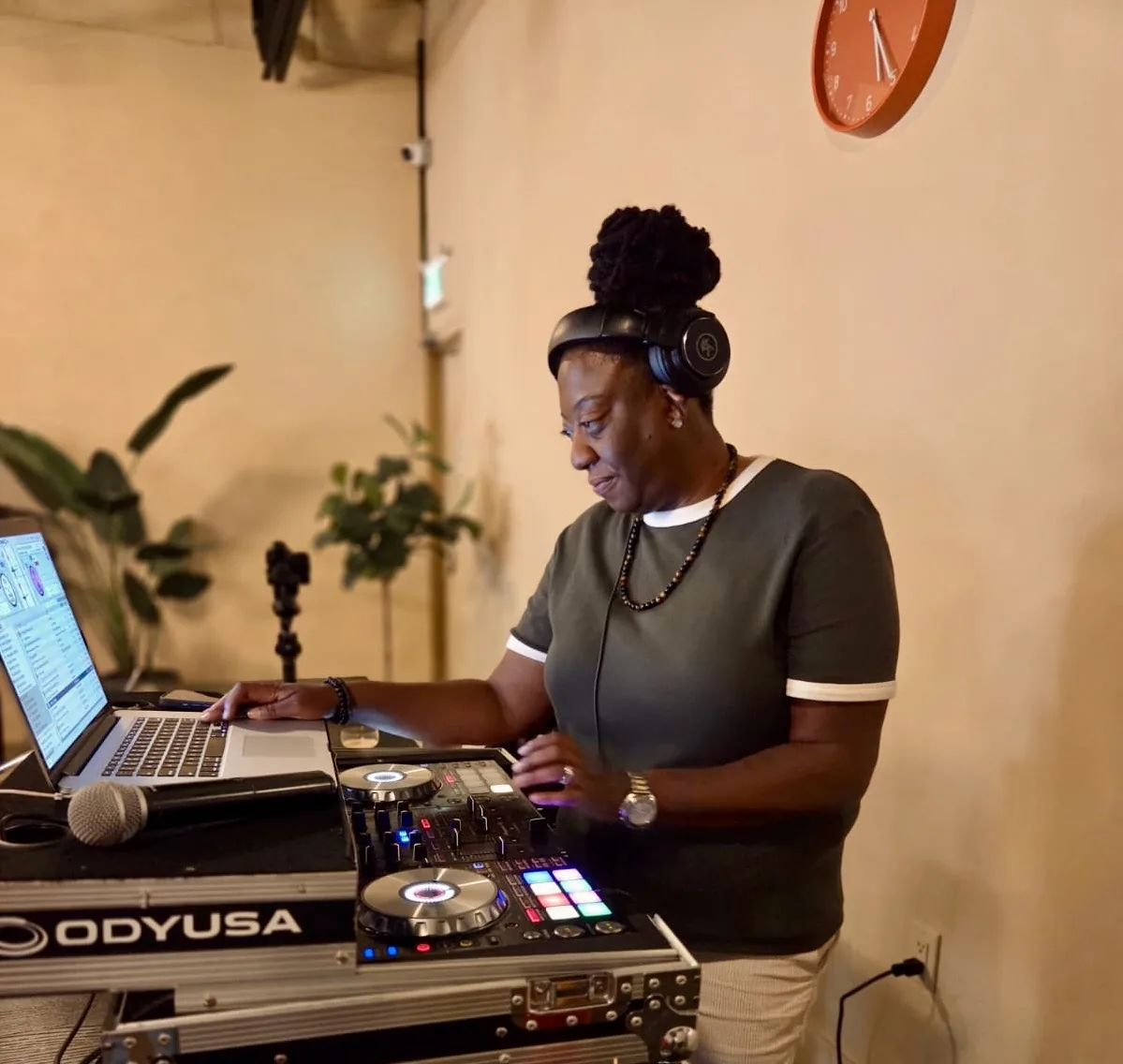 DJ JJ Rock wearing a green top and headphones at a laptop and DJ controller