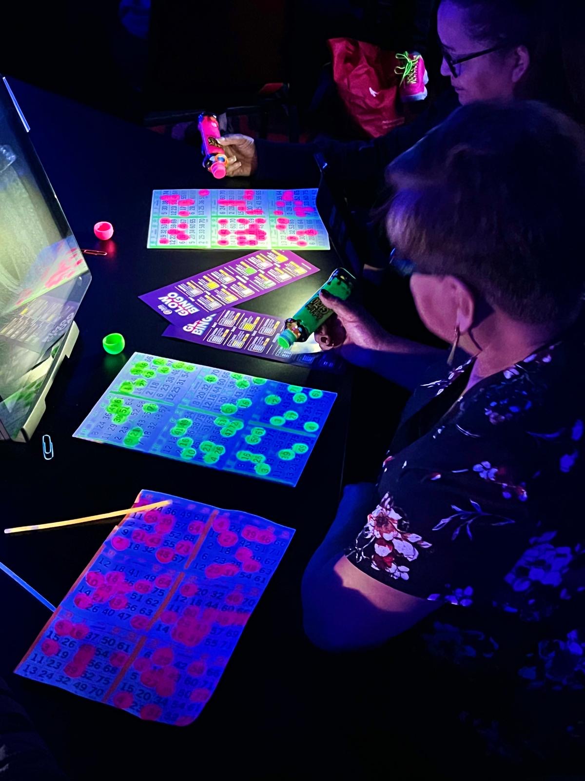 Guests marking glowing bingo cards with colourful dabbers during the Toronto Glow Bingo event