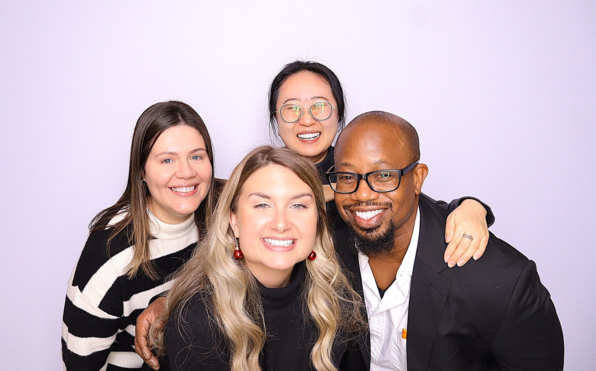 Four guests smiling together in a photo booth against a light backdrop