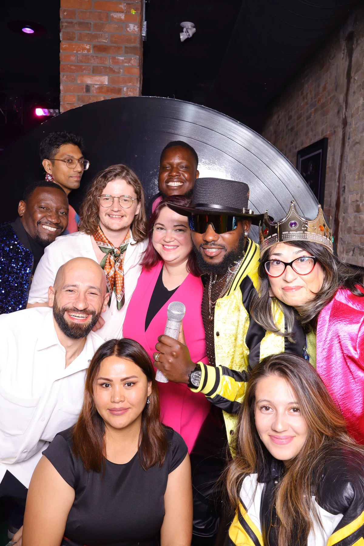 A group of friends smiling with photo booth props beside a record backdrop