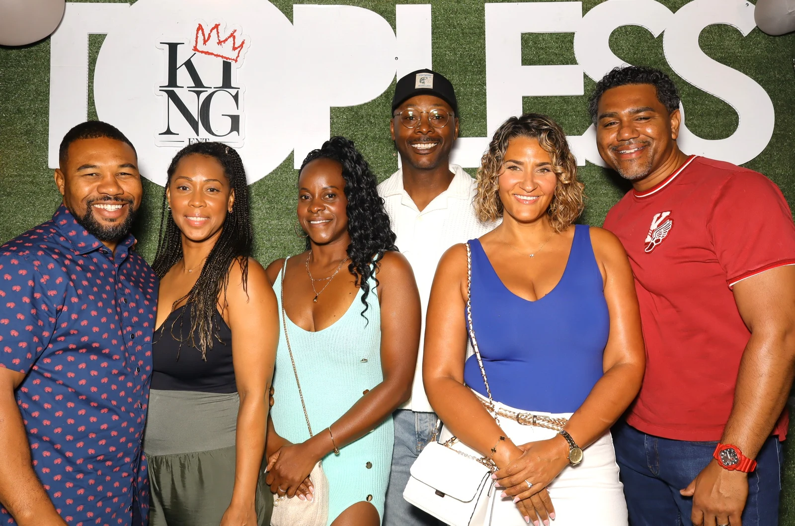 Six guests smiling together in front of a green event backdrop