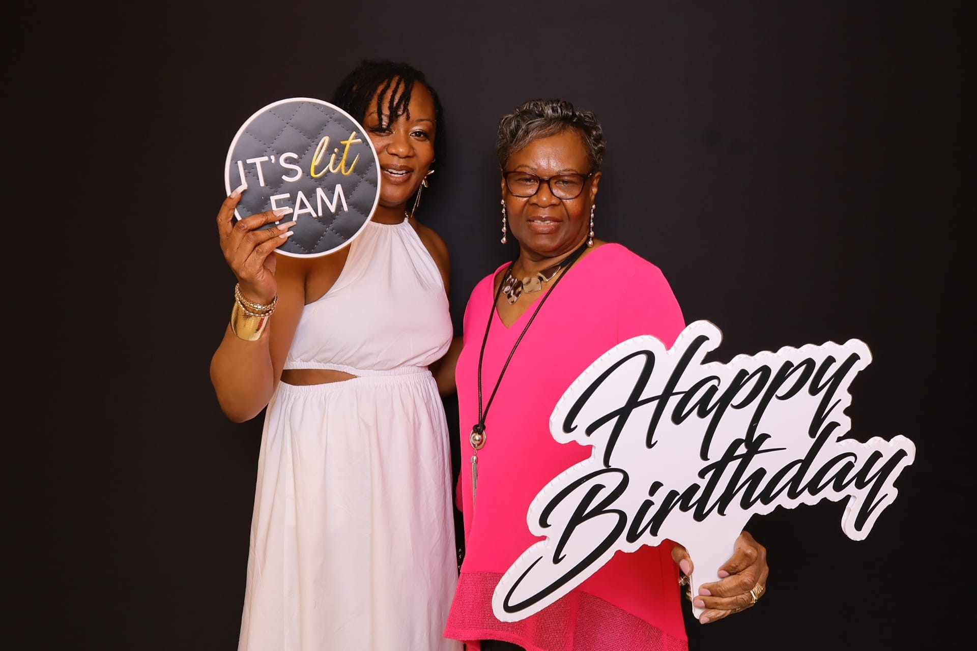 Two guests holding Happy Birthday and It's Lit Fam props at the photo booth